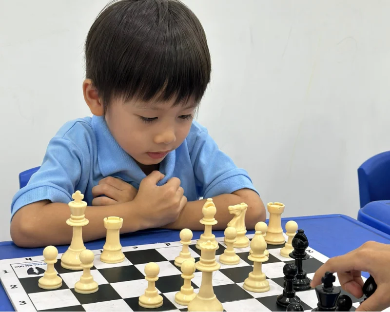 Bé trai đang tập trung chơi cờ vua để rèn luyện tư duy logic
